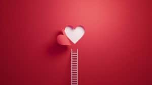 White ladder leaning on red wall with cut out heart shape.