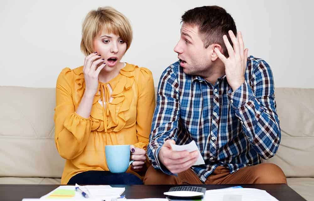 A young couple checking over their finances together, and looking shocked.