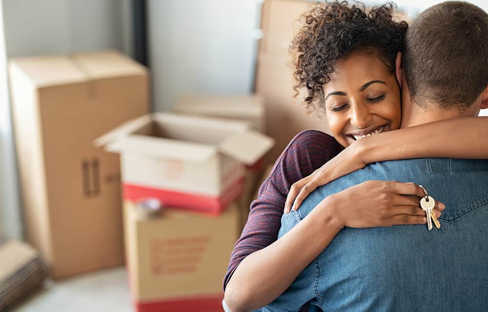 A man and women hug, celebrating moving into their first home.