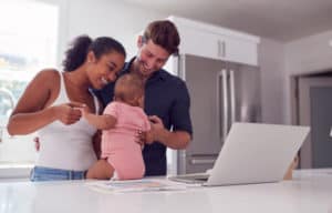 A young family gathered around a laptop on their kitchen countertop