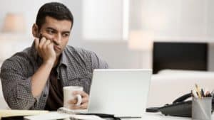 Hispanic man using laptop in home office and drinking coffee