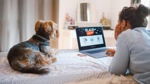 Woman buying electronics online at Black Friday while relaxing at the bed with her dog
