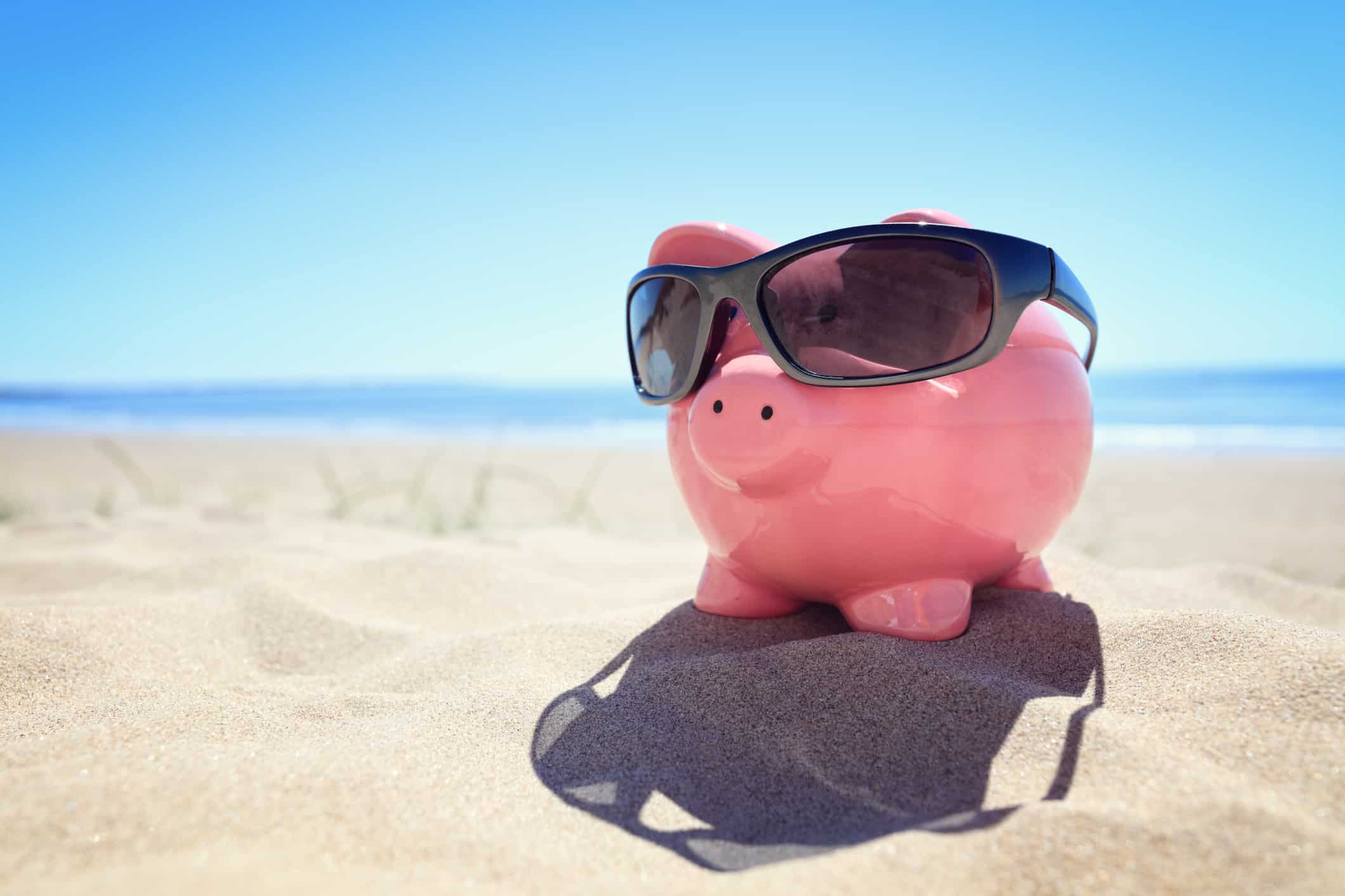 A piggy bank wearing sunglasses, at the beach.
