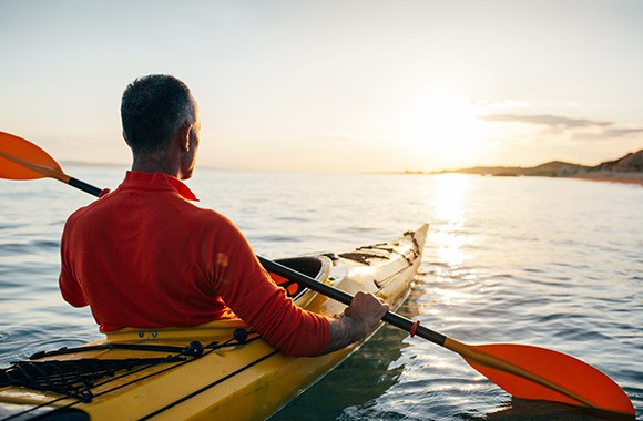 Rear view of active middle aged man enjoy paddling kayak on the sunset sea.