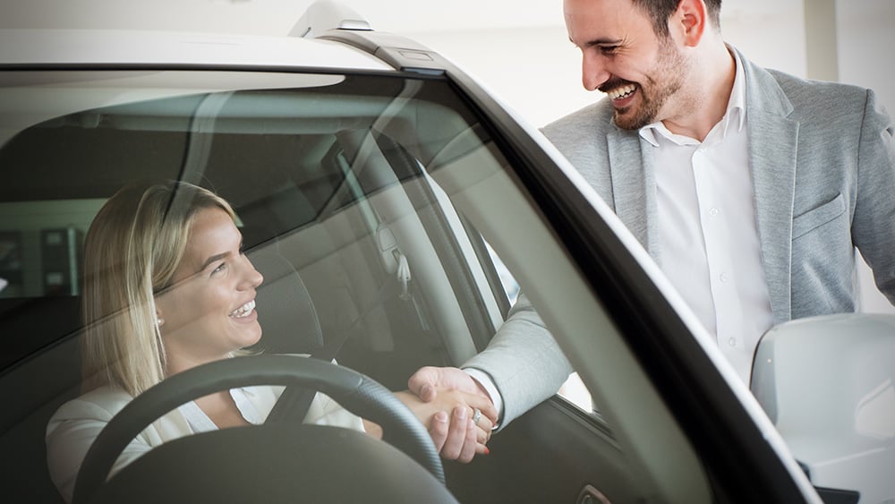 A happy young customer shakes hand with the car dealer who is selling her a new car