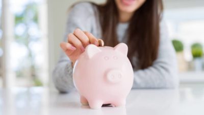 Young woman smiling putting a coin inside piggy bank as savings for investment