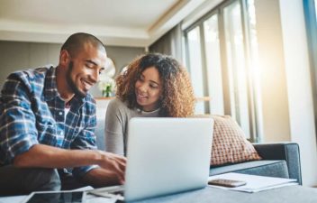 A young couple take use a laptop together in their living room