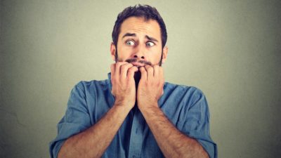 Anxious young man biting his nails fingers