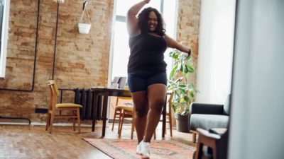 Happy woman with excess weight smiling and dancing alone in sports clothes