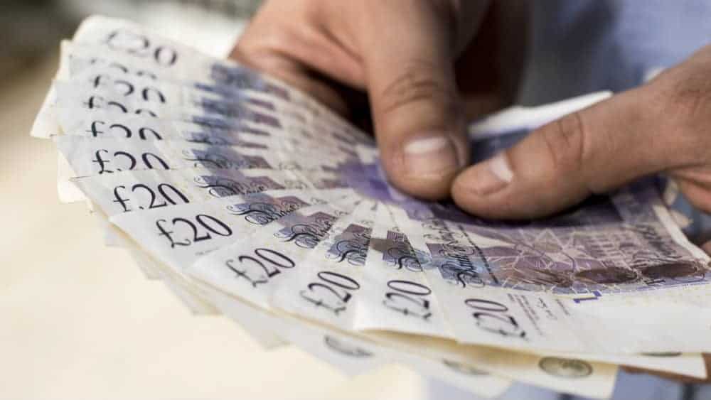 A person holding onto a fan of twenty pound notes