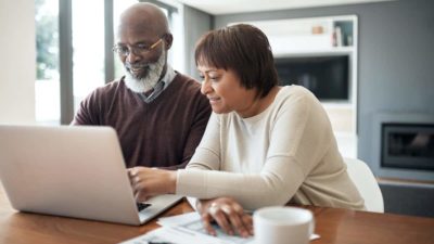 happy senior couple using a laptop in their living room to look at their financial budgets