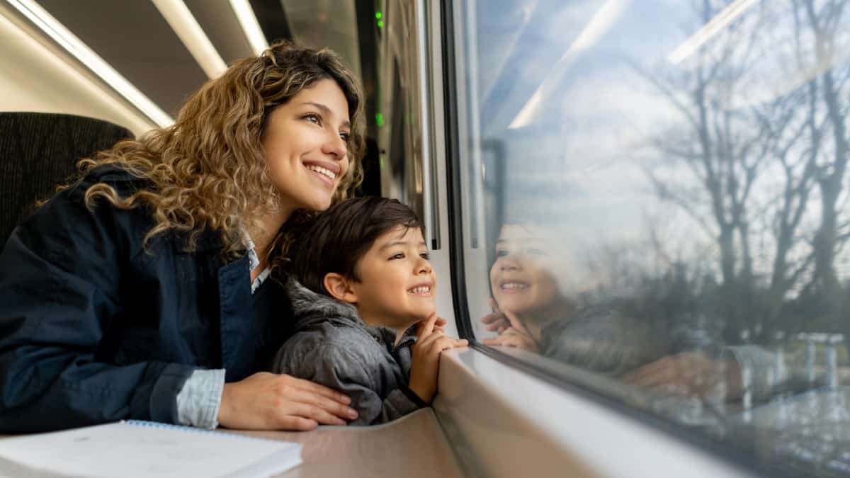Happy single mother and son looking at the window view both smiling while traveling by train