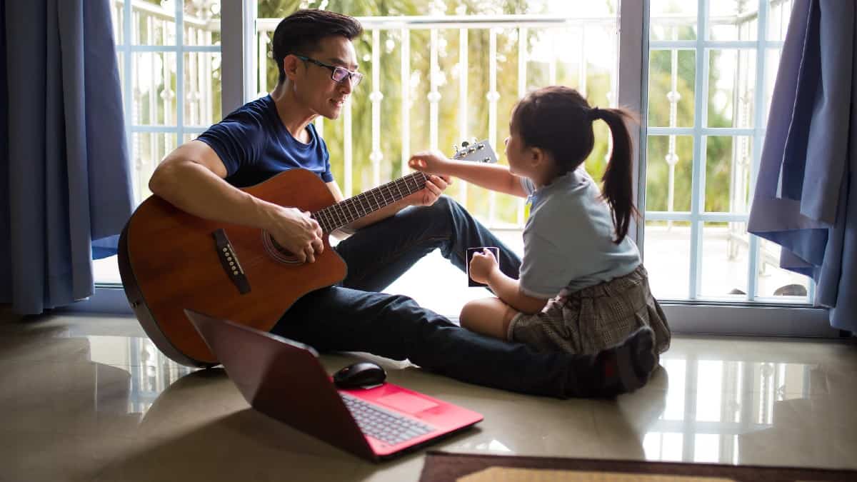 Father playing guitar on the floor with daughter sitting beside him.