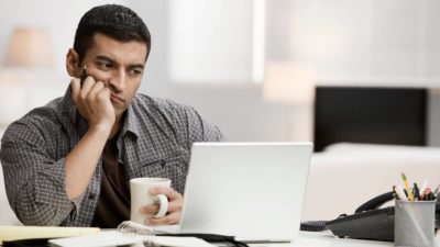 Hispanic man using laptop in home office and drinking coffee