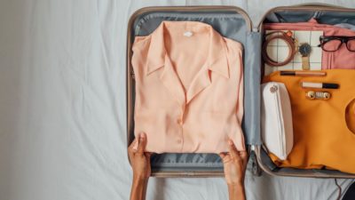 Hands of woman putting elegant blouse in a suitcase.