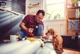 Man with dog building kitchen cabinets and using a cordless drill