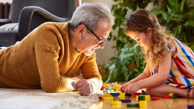 Granddaughter playing with wooden block and granddad watching