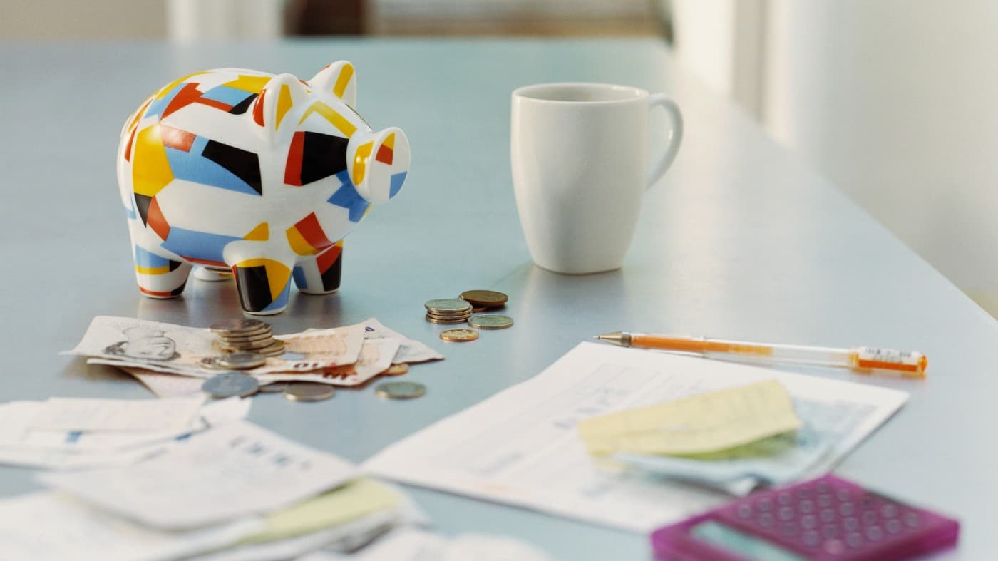 Piggybank, British Currency, Calculator, Receipts and a Mug on a Table -