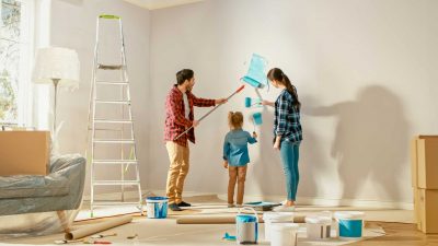 Beautiful Young Family are Showing How to Paint Walls to Their Adorable Small Daughter. They Paint with Rollers that are Covered in Light Blue Paint. Room Renovations at Home.