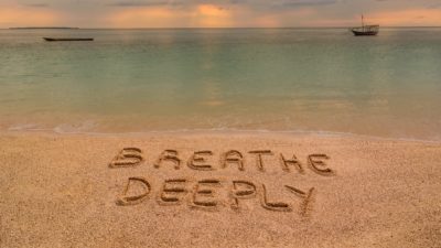 A beach at sunset where there is an inscription on the sand "Breathe Deeeply".