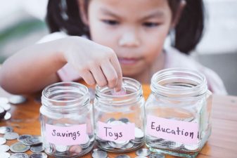 Cute asian little child girl putting coin into glass bottle in the garden