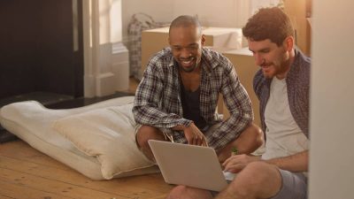 Two men moving into a new home, looking at laptop