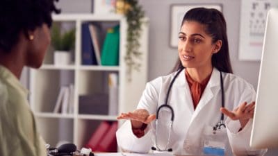 Female Doctor In White Coat Having Meeting With Woman Patient In Office