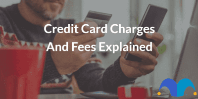 Man sat at laptop computer using credit card to pay online using mobile phone with the text “Credit card charges and fees explained” and The Motley Fool jester cap logo