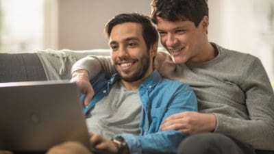 Happy male couple looking at a laptop screen together