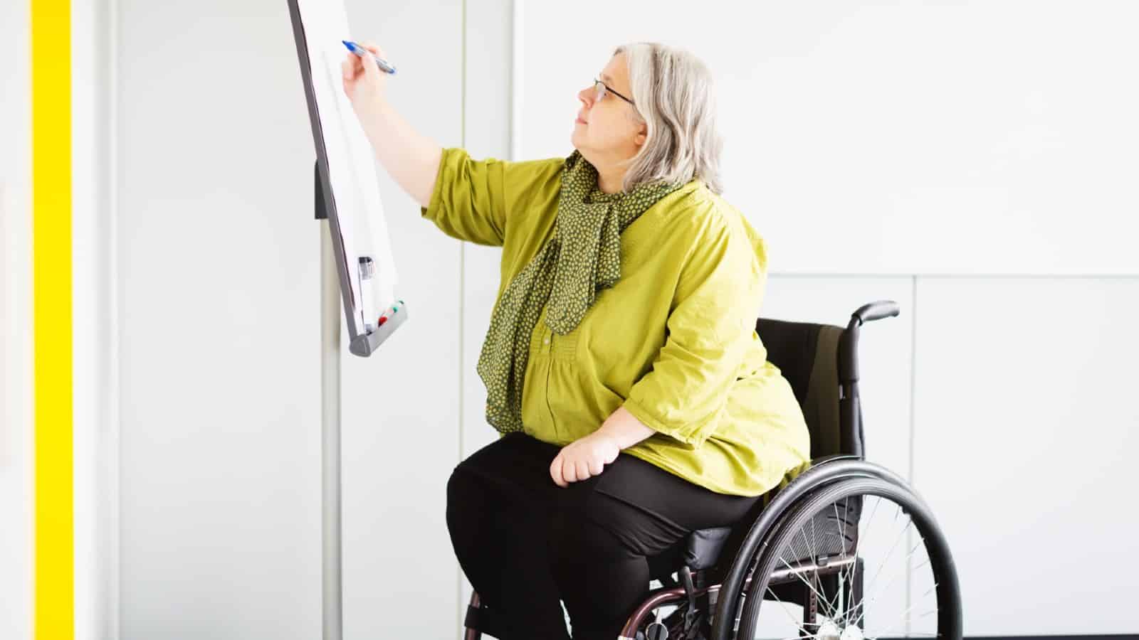 Middle-aged lady in wheelchair writing on whiteboard