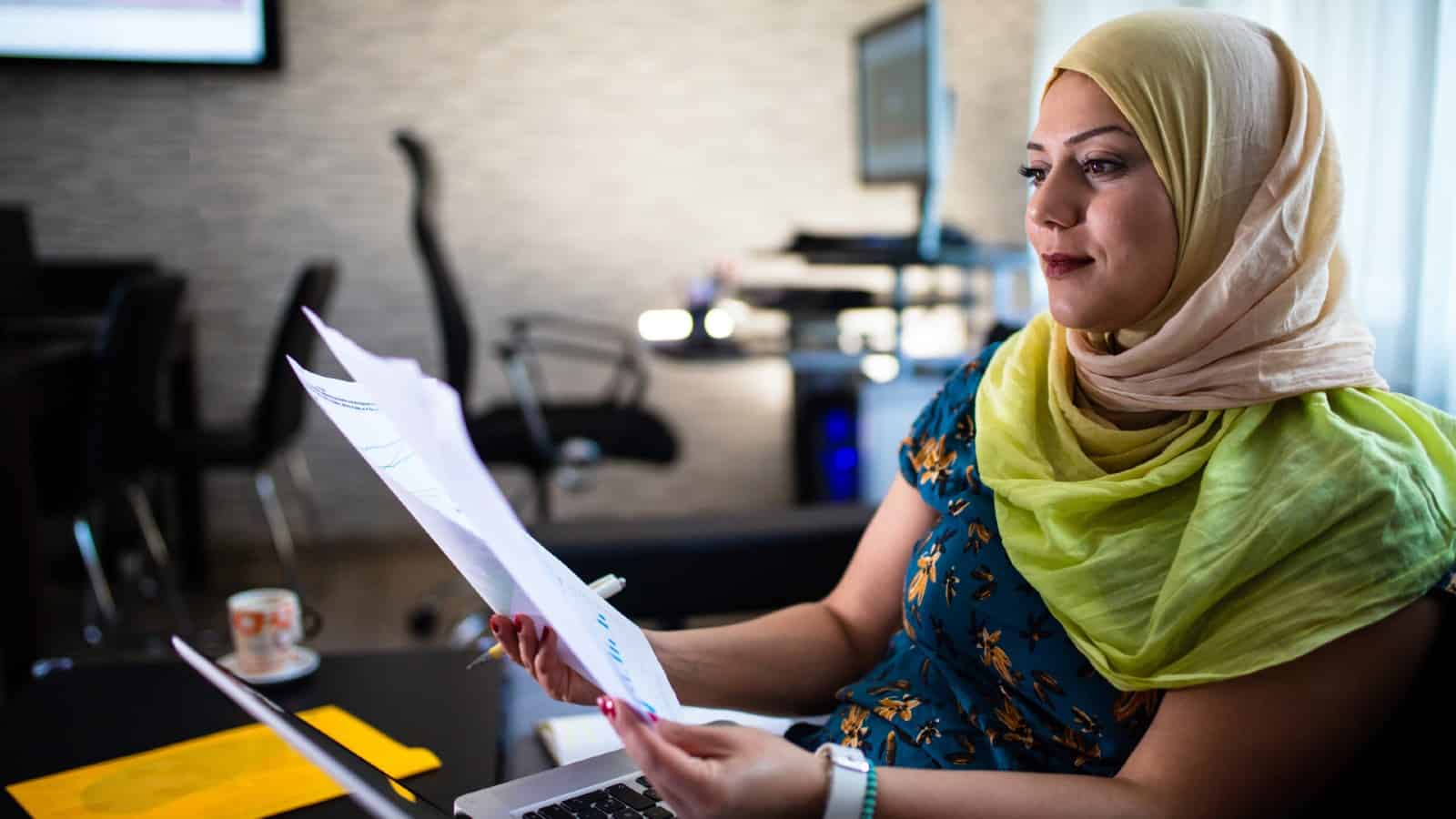 Lady wearing a head scarf looks over pages on company financials