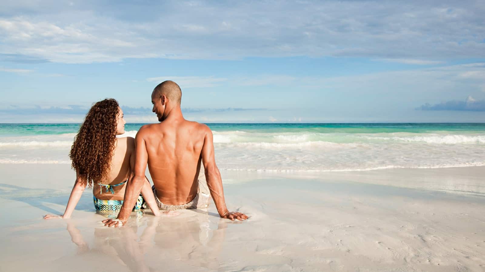 Young mixed-race couple sat on the beach looking out over the sea