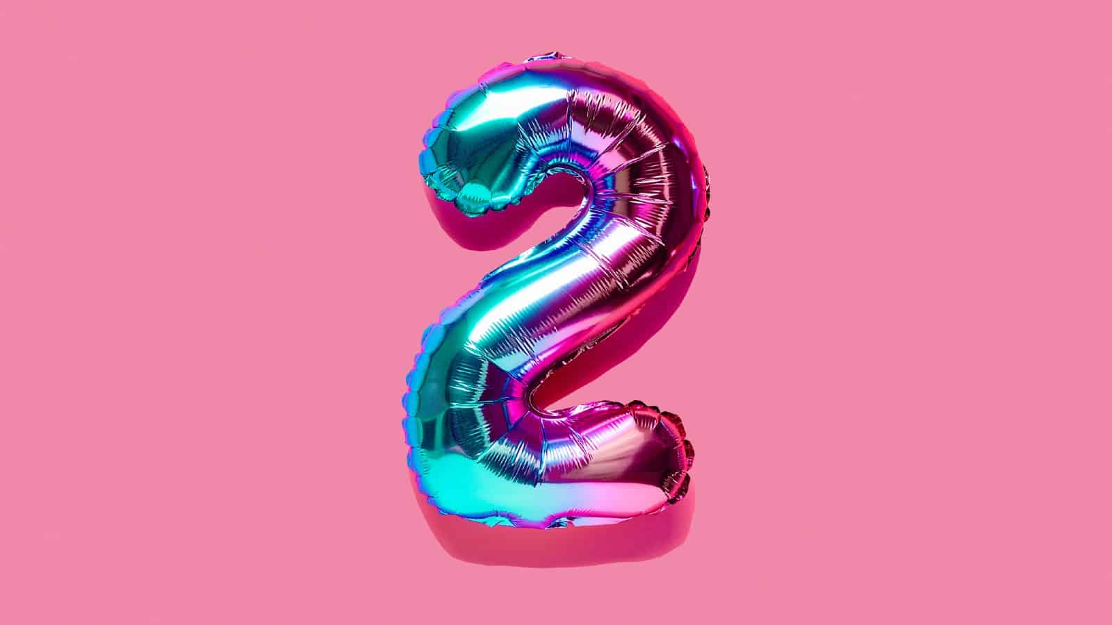 Rainbow foil balloon of the number two on pink background