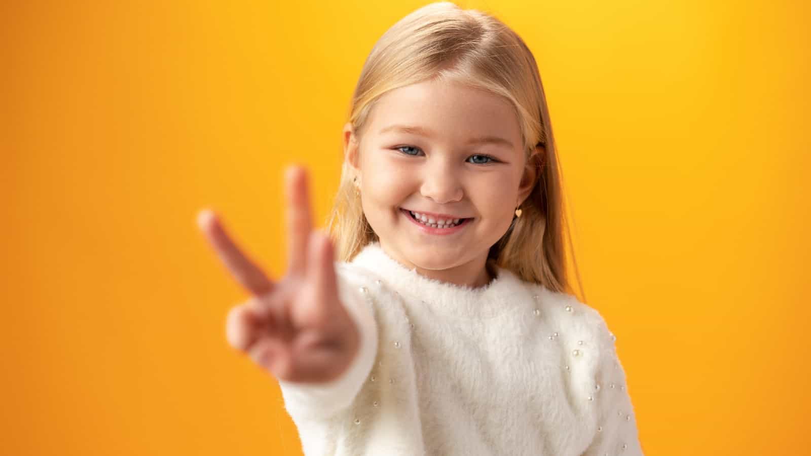 Young Caucasian girl showing and pointing up with fingers number three against yellow background