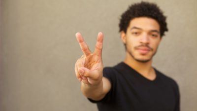 A young black man makes the symbol of a peace sign with two fingers