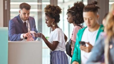 Smiling black woman showing e-ticket on smartphone to white male attendant at airport