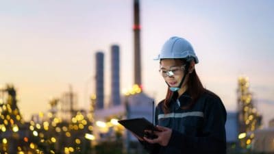 Petrochemical engineer working at night with digital tablet inside oil and gas refinery plant