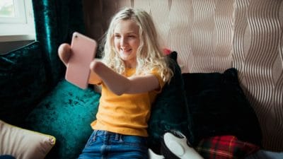 A confident young girl sitting on her own, smiling for a selfie.