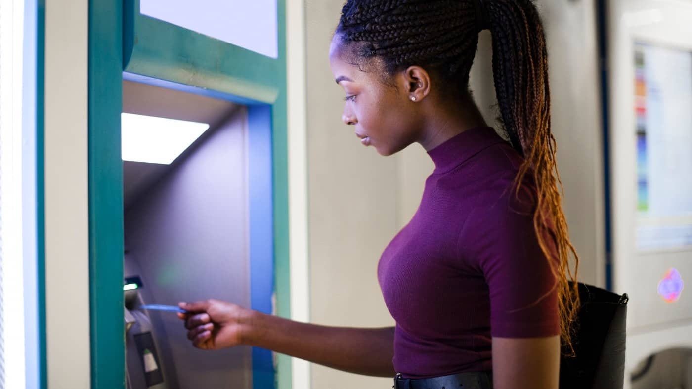 Young Black woman using a debit card at an ATM to withdraw money