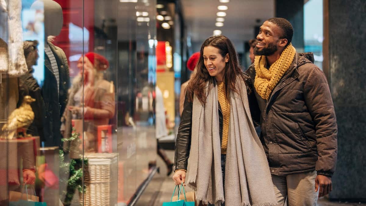 Front view of a mixed-race couple walking past a shop window and looking in.