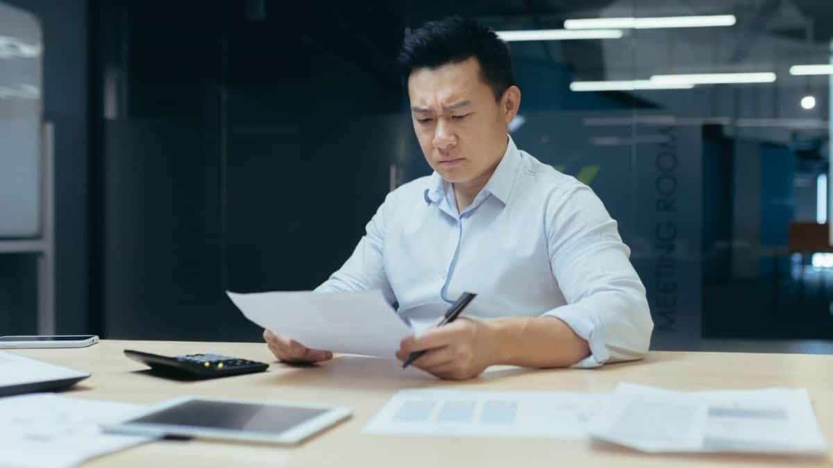 Asian man looking worried while studying papers on his desk in an office