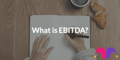 A notebook spread open with two hands preparing to write, with the text, "What is EBITDA?".