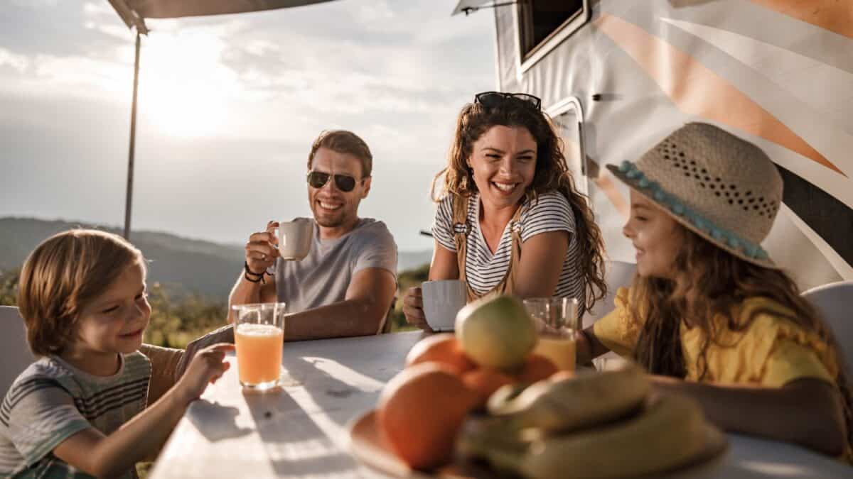 Smiling family of four enjoying breakfast at sunrise while camping