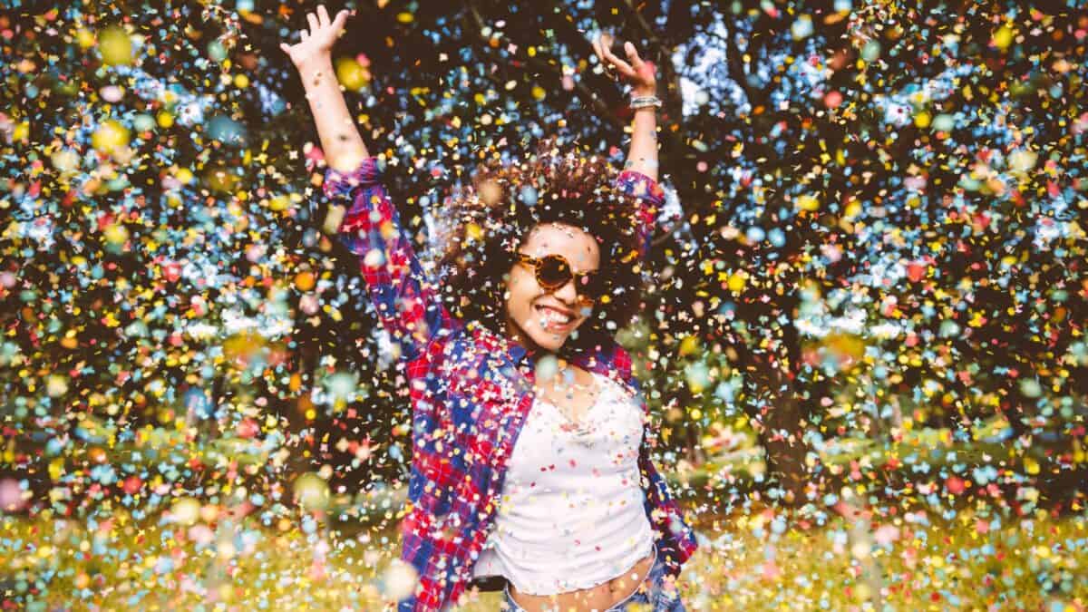 Young mixed race woman jumps for joy in a park as confetti falls around her
