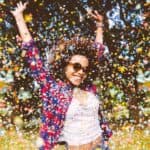 Young mixed-race woman jumping for joy in a park with confetti falling around her