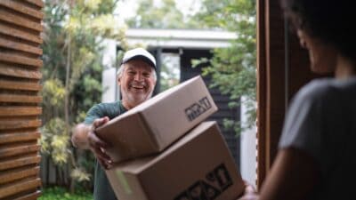 Middle-aged white male courier delivering boxes to young black lady