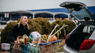 Young happy white woman loading groceries into the back of her car