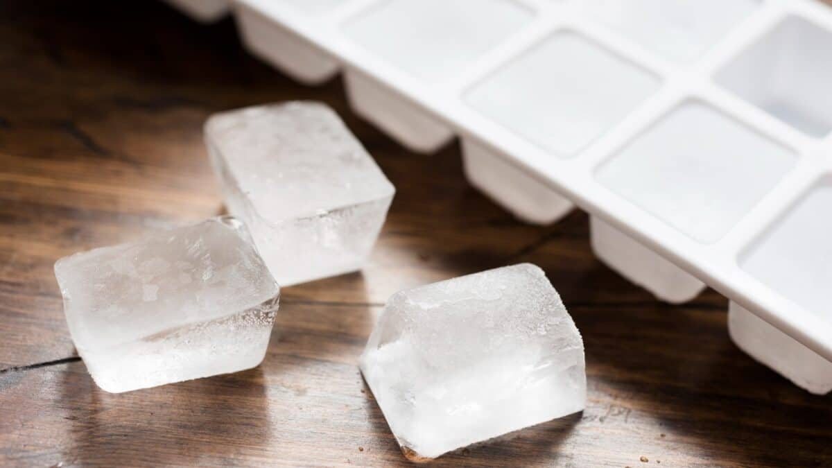 Ice cube tray filled with ice cubes and three loose ice cubes against dark wood.