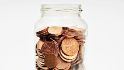 UK coins (1p & 2p) in a savings glass jar against a plain studio background.