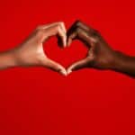 Two multiracial girls making heart sign against red background
